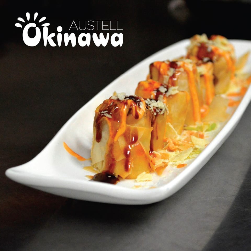 Okinawa's crispy spring rolls drizzled with sweet and spicy sauces on a white platter.