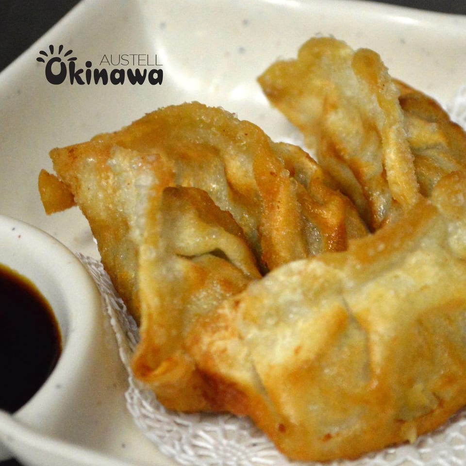 Golden-brown fried gyoza dumplings with a side of dark dipping sauce on a white plate.
