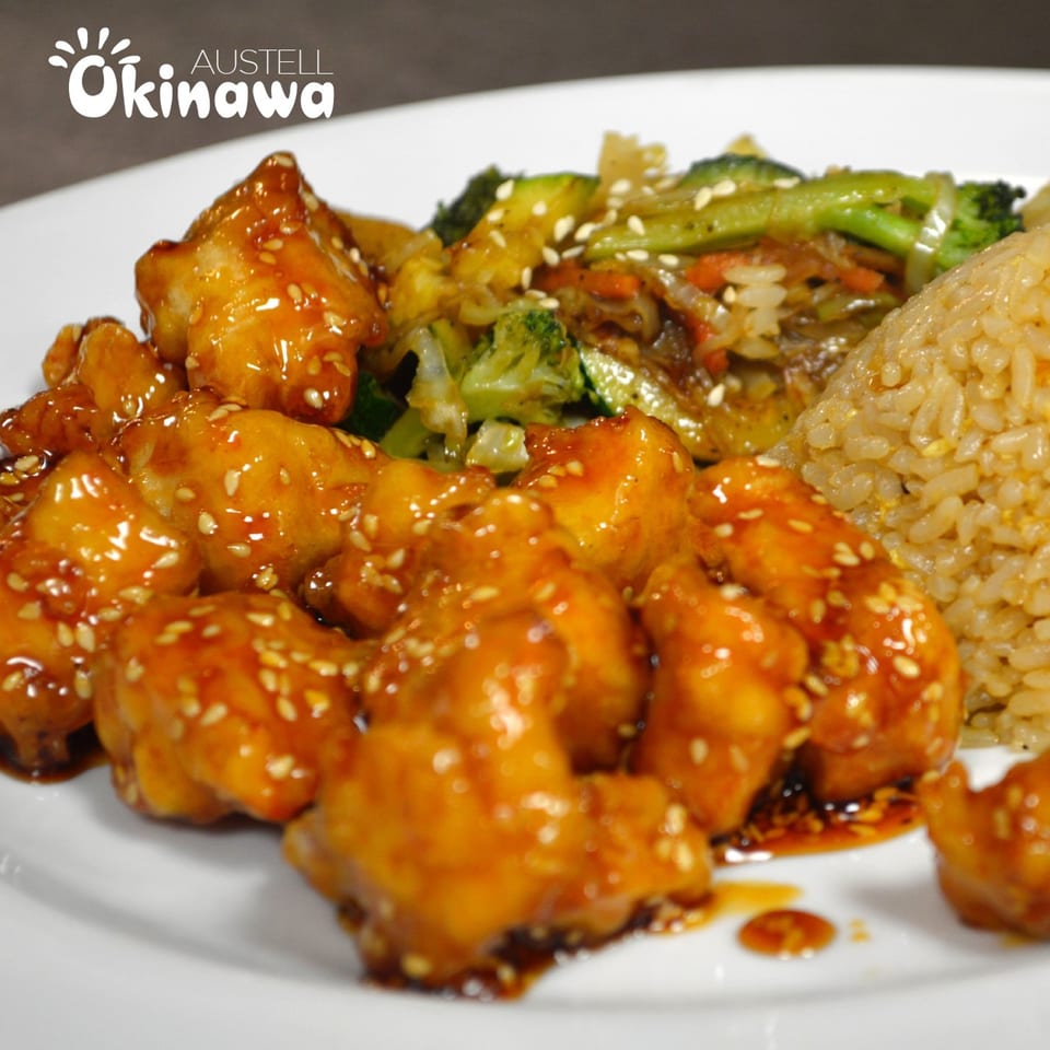 Okinawa's sesame chicken with fried rice and stir-fried vegetables on a white plate.