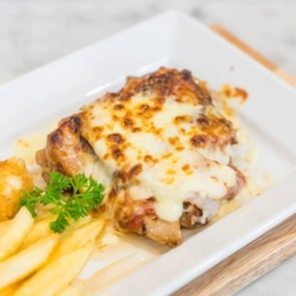 Cheesy chicken with french fries and parsley on a white rectangular plate.