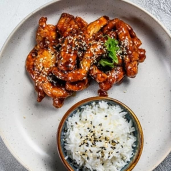 Teriyaki chicken with sesame seeds and a side of white rice in a bowl.