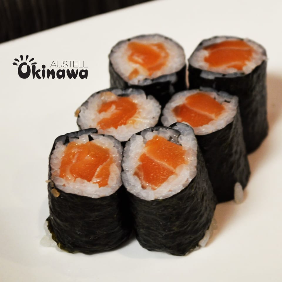 Six salmon maki sushi rolls with nori, rice, and bright orange salmon on a white plate.